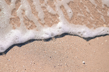 Wet sand and sea foam on the beach, sea waves. Summer time, vacation travel concept. Copy space for your text
