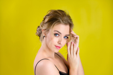 Glamorous beauty portrait side view of a pretty blonde model with excellent makeup and a beautiful hairstyle on a yellow background in the studio. The concept of cosmetics, fashion and style.