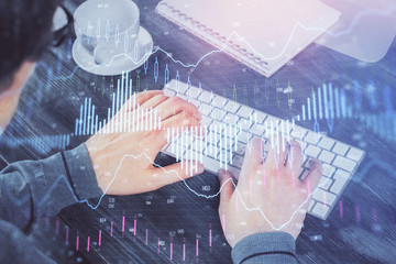 Double exposure of graph with man typing on computer in office on background. Concept of hard work.