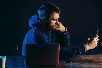 guy commiting crime in dark space, sit with laptop, gadgets. hacker finding and exploiting weakness in computer system to gain access. spreading computer viruses, online bullying