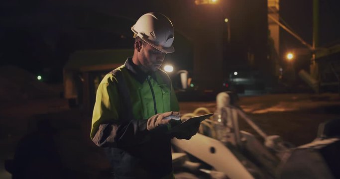 African night shift worker controlling gravel stone loading and transportation using digital tablet
