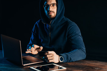 guy commiting crime in dark space, sit with laptop, gadgets. hacker finding and exploiting weakness...