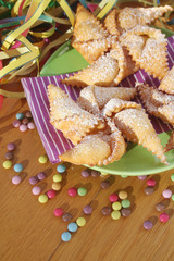 Traditional carnival pastry, chiacchere or crostoli, bugie, cenci in shape of a toy windmill on wooden background with coloful decorations