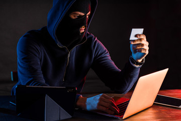 young caucasian hacker man in the hood of pullover sit holding bank card, going to crack algorithm...