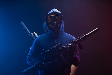 Male hoodie hacker wearing mystery mask hold gun in hands, man with weapon behind him. cyber attack...