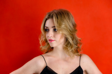 Fototapeta premium The concept of cosmetics, fashion and style. Glamorous beauty front view portrait of a pretty model with blond hair with great makeup and a beautiful hairstyle on a red background in the studio.