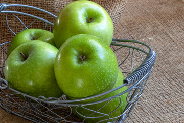 Pommes Granny Smith dans un panier de métal sur toile de jute