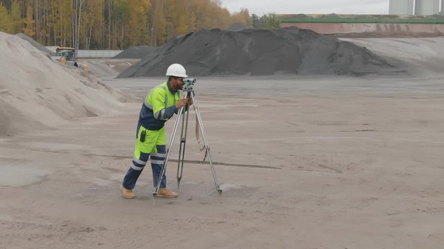 Afro-american geodesist using level unit doing landscape work on construction site
