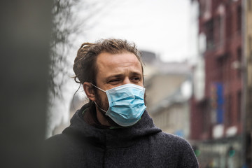 Handsome young European man in winter clothes on the street with a medical face mask on. Closeup of...