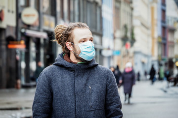 Naklejka premium Handsome young European man in winter clothes on the street with a medical face mask on. Closeup of a 35-year-old male in a respirator to protect against infection with influenza virus or coronavirus