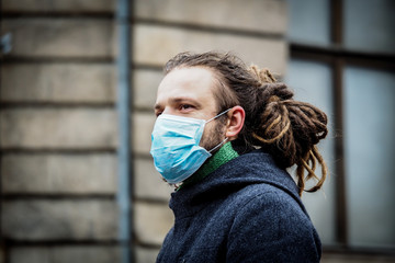 Handsome young European man in winter clothes on the street with a medical face mask on. Closeup of...