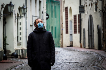 Fototapeta na wymiar Handsome young European man in winter clothes on the street with a medical face mask on. Closeup of a 35-year-old male in a respirator to protect against infection with influenza virus or coronavirus