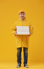 Full length portrait of adult delivery man holding pizza boxes and smiling at camera standing against yellow background