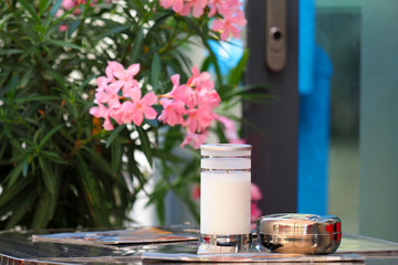 Little table of street cafe, menu, ashtray, candle. Blooming pink oleander in the background,...