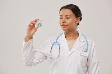 Waist up portrait of beautiful female doctor holding pill bottle while standing against white background, copy space