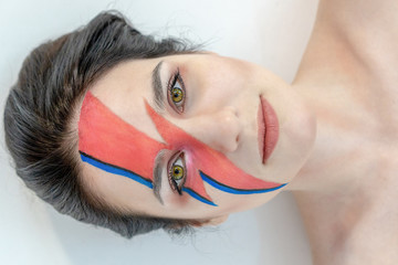 Close-up portrait of a beautiful girl with creative make-up, who lies on the floor in the studio.