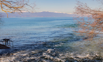 The lush waters of the springs flow into the lake with their incredible shades. Against the background of trees and a solitary table in the water. And winter hills in the distance.  Northern Macedonia