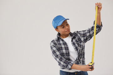 Waist up portrait of pretty female worker holding measuring tape while standing against white background, copy space