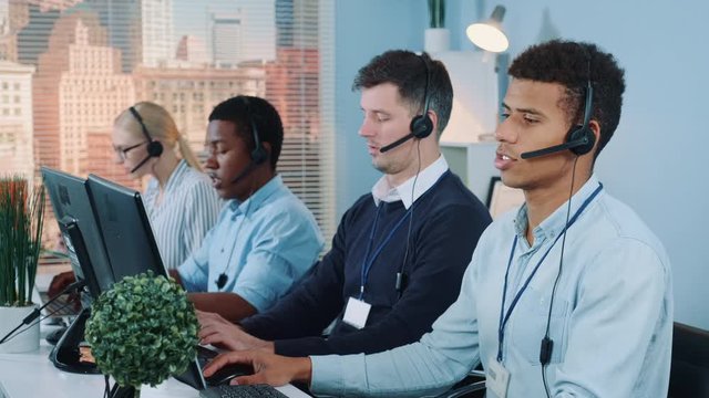 Medium shot of Multiracial call center agents talking to the clients in headset. There are skyscrapers in the background.