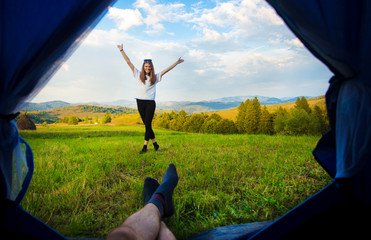 Man lying in tent and looking for his girlfriend with hands up, view from inside of tent. Hiking in mountains.