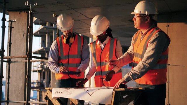 Three engineers work with a blueprint in a building. Construction contractor working on a construction site.
