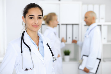 Fototapeta premium Doctor woman in clinic with colleagues at the background. Hispanic or latin american staff in medicine