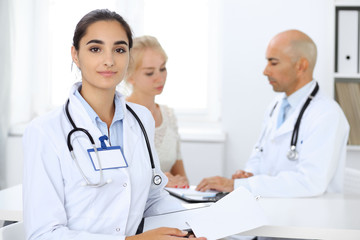 Doctor woman in clinic with colleagues at the background. Hispanic or latin american staff in medicine