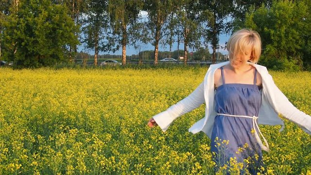 an attractive young blonde woman walks through a field of rapeseed, smiling and spinning merrily. Slow motion