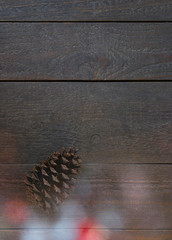 Christmas card with a fir cone and beautiful colourful christmas lights in front of a wooden background