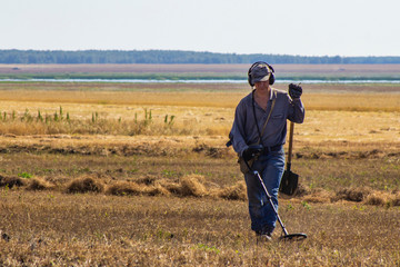 black archaeologist with a metal detector looking for treasure in a field, close-up on a plowed pasture