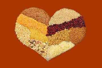 Different kind of cereals, grain and seeds, setting in the heart shape on red background. Natural organic vegetarian or vegan concept, healthy food.