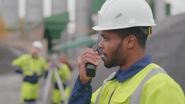 Side view of african manager with walkie talkie supervising work of crushed stone quarry.