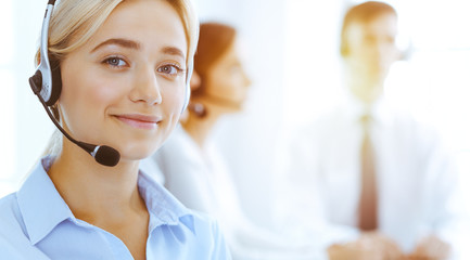 Group of diverse phone operators at work in sunny office. Handsome business woman with headphones consulting clients. Call center and business people concept