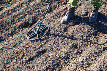 black archaeologist with a metal detector looking for treasure in a field, close-up on a plowed...