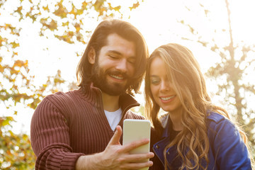 Young couple using cellphone in autumn colored park.