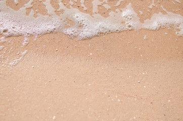 Wet sand and sea foam on the beach, sea waves. Summer time, vacation travel concept. Copy space for your text