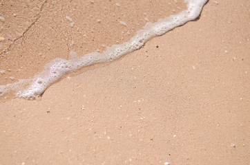 Wet sand and sea foam on the beach, sea waves. Summer time, vacation travel concept. Copy space for your text