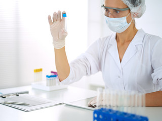 Professional female scientist in protective eyeglasses researching tube with reagents in laboratory. Concepts of medicine and research