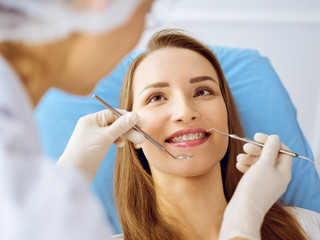 Smiling young woman with orthodontic brackets examined by dentist at dental clinic. Healthy teeth and medicine concept