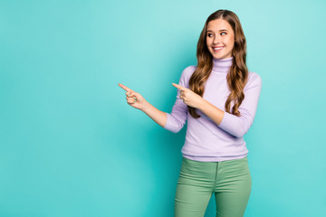 Photo of funny pretty lady indicate fingers look empty space offer novelty product sale prices addicted shopper wear purple sweater green trousers isolated pastel teal color background