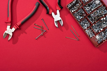 Top view of tool box with pliers and nails on red surface