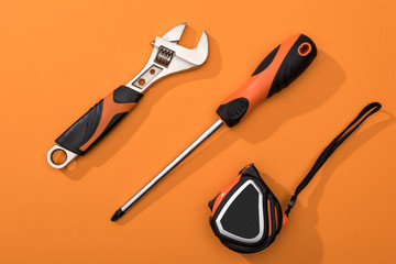Top view of wrench, screwdriver and measuring tape on orange background