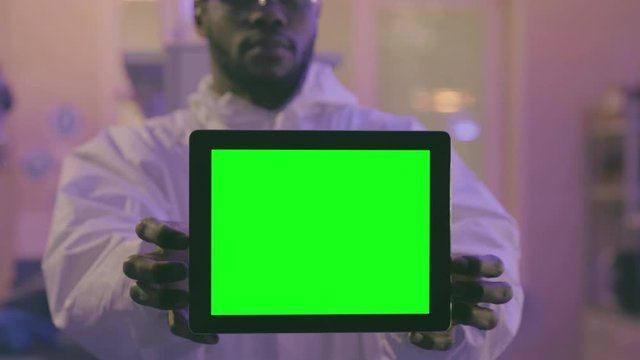 Young afro-american scientist showing digital tablet with green screen at camera