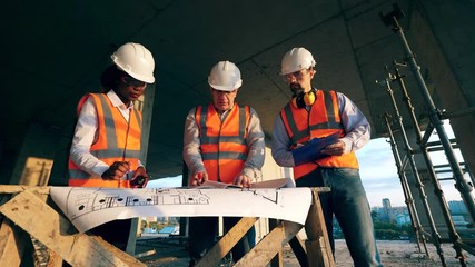 Multiethnic engineers, architects discussing construction plan. Engineers work with a blueprint on a table on a construction site. - Powered by Adobe