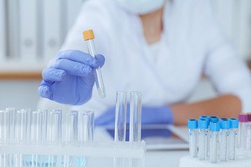 Close-up of professional female scientist in protective eyeglasses making experiment with reagents in laboratory. Medicine and research concept