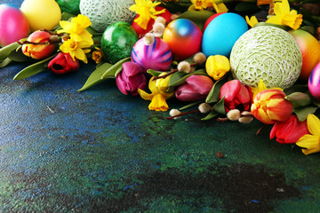 Easter eggs and tulips and daffodils on rustic background. Springtime decoration
