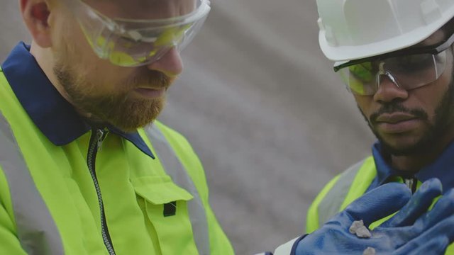Multicultural industrial workers examining gravel of different fraction type.