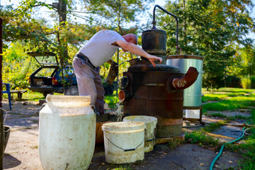 Fototapeta na wymiar Man is washing fruit marc from distillation apparatus after cooking and making domestic alcohol liquor