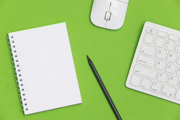 Office desk with notepad, keyboard and supplies on green background. Top view with copy space for...