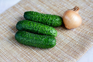 Three cucumbers and an onion on the table on a wicker napkin